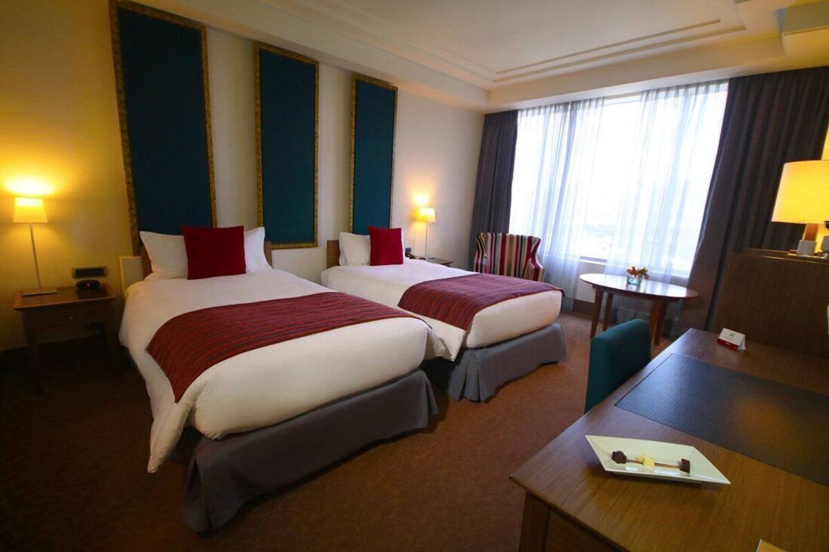 Een hotelkamer met twee bedden, een bureau, een stoel en een tafeltje met een lamp.