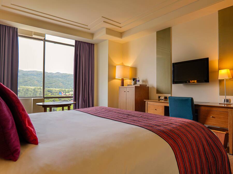 Een hotelkamer met een groot bed, een bureau, een stoel, een televisie en uitzicht op het omliggende landschap.