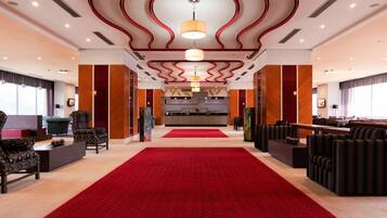 A hotel lobby with a red carpet, seating areas, and a reception desk.
