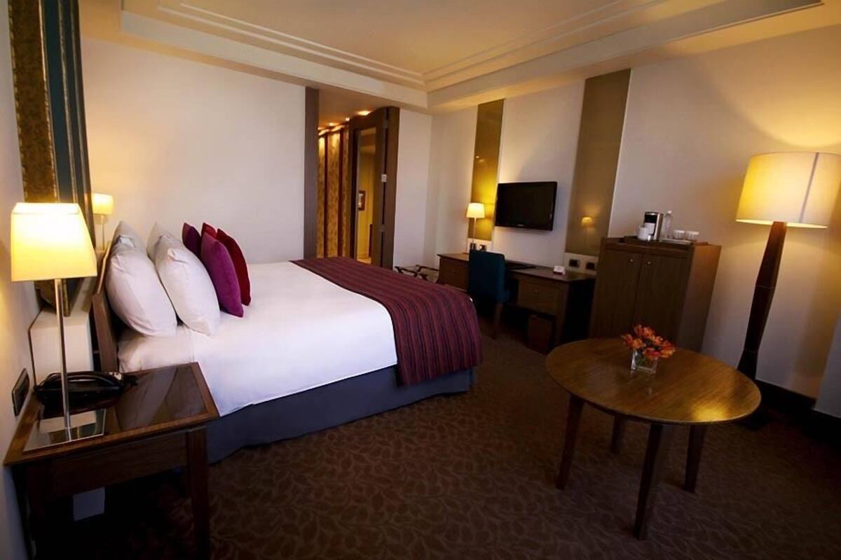 Een hotelkamer met een bed, nachtkastjes, een bureau, een televisie en een ronde tafel met bloemen.