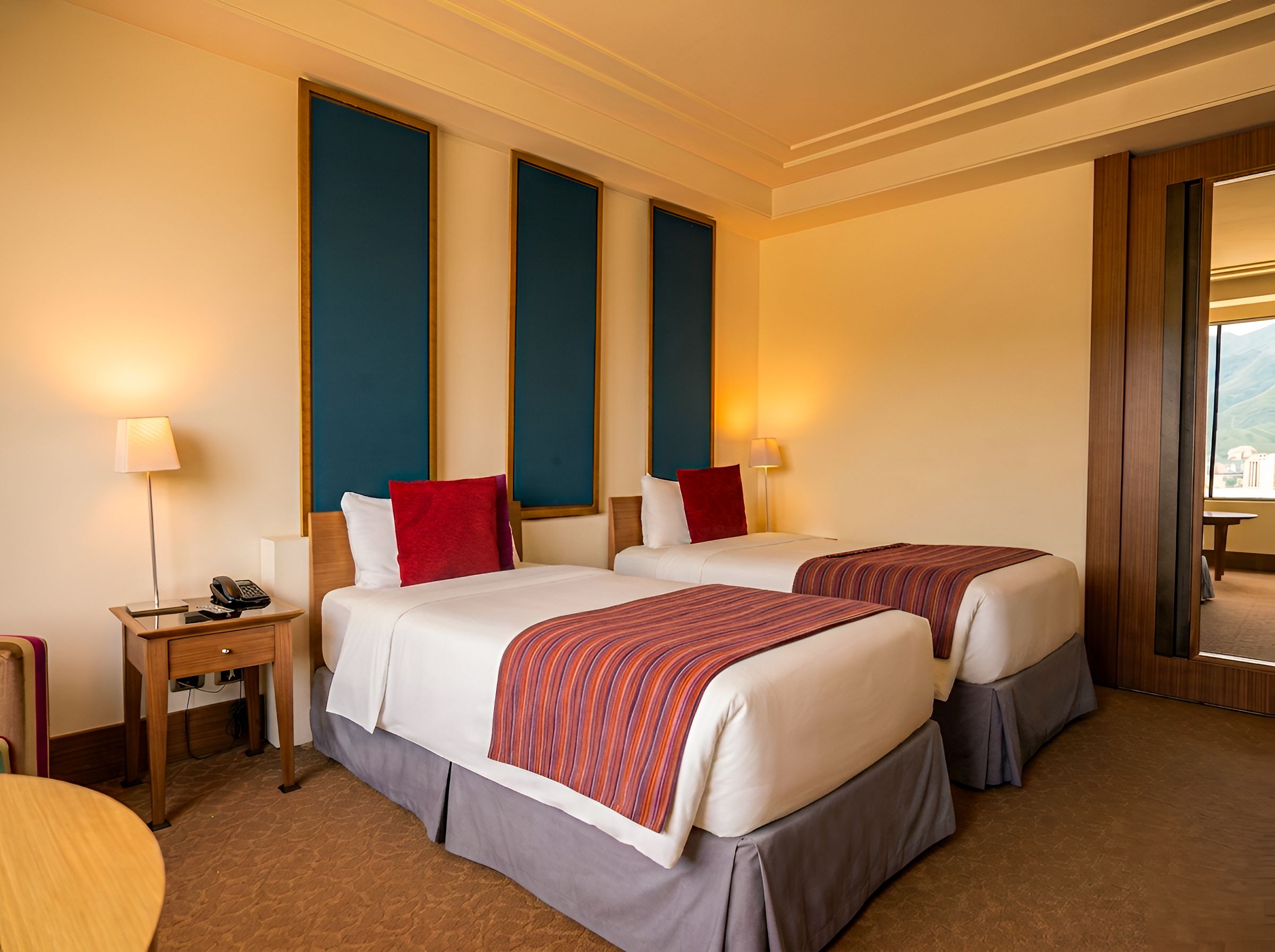 A hotel room with two beds, a desk with a telephone, and a view of the outdoors.
