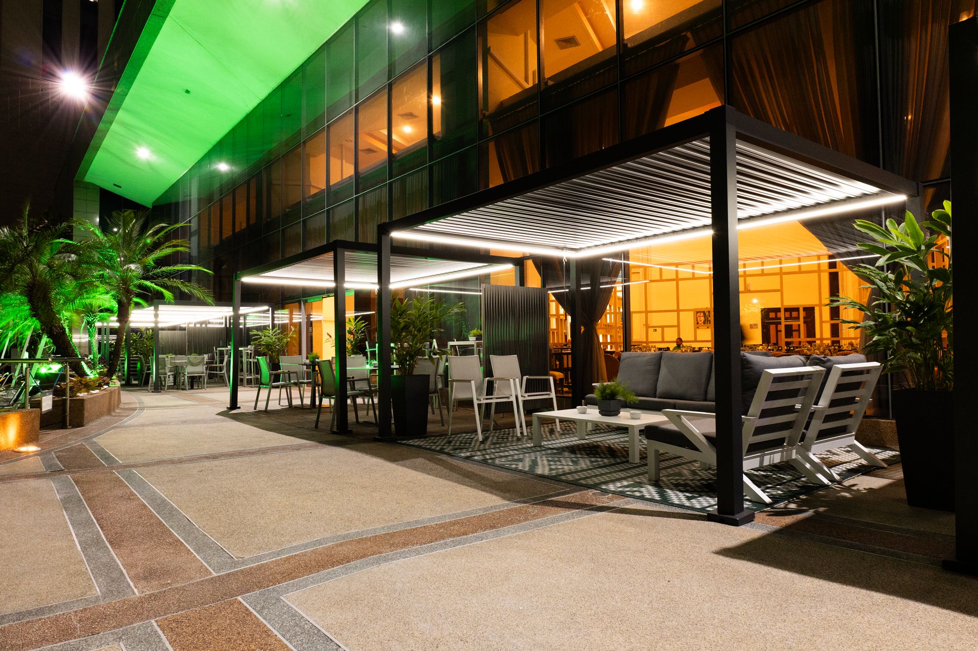 An outdoor seating area with tables and chairs, a covered section with a patterned ceiling, and potted plants.