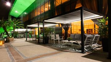 An outdoor seating area with tables and chairs, a covered section with a patterned ceiling, and potted plants.