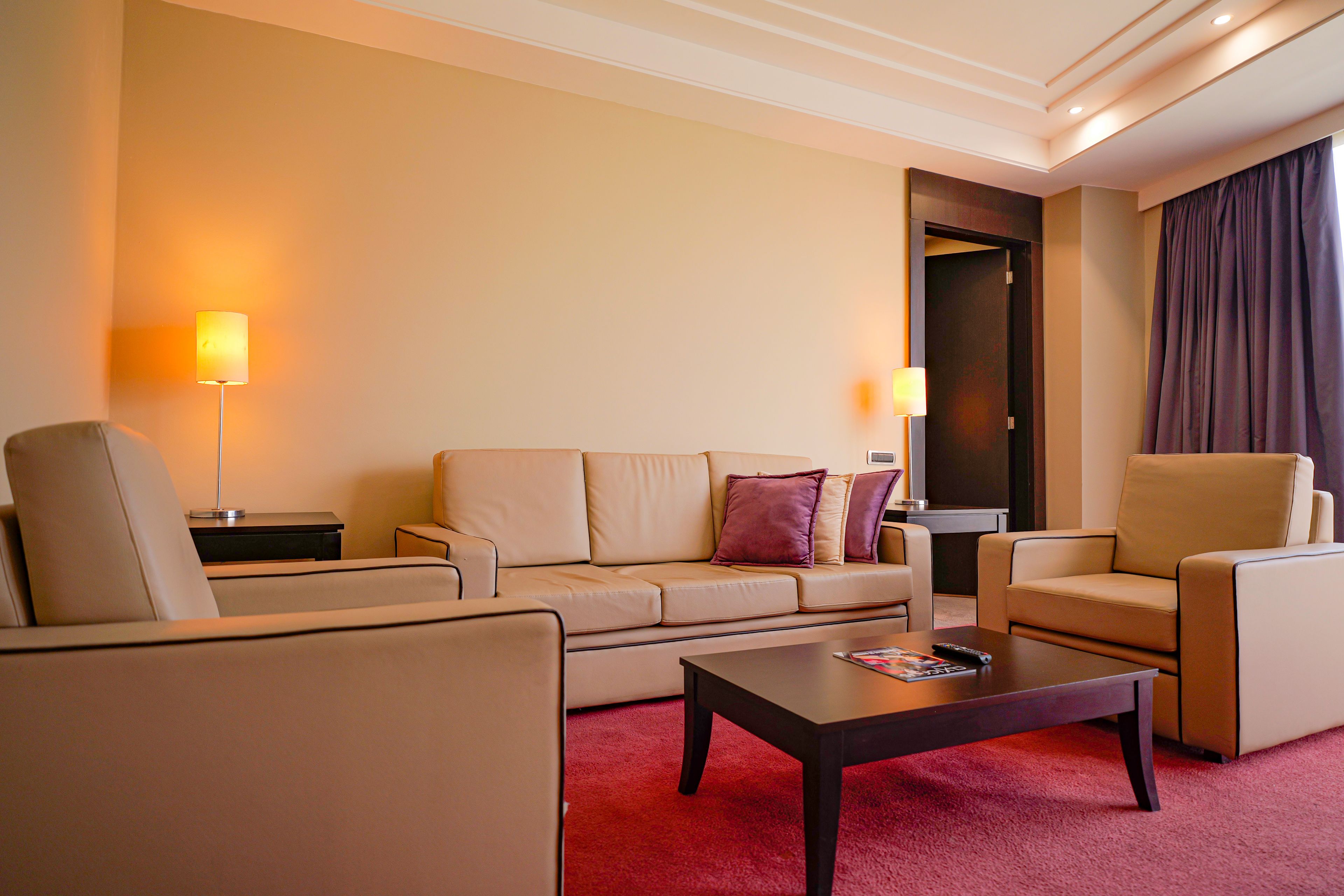 A hotel room with a beige sofa, a matching armchair, a coffee table, and two floor lamps.