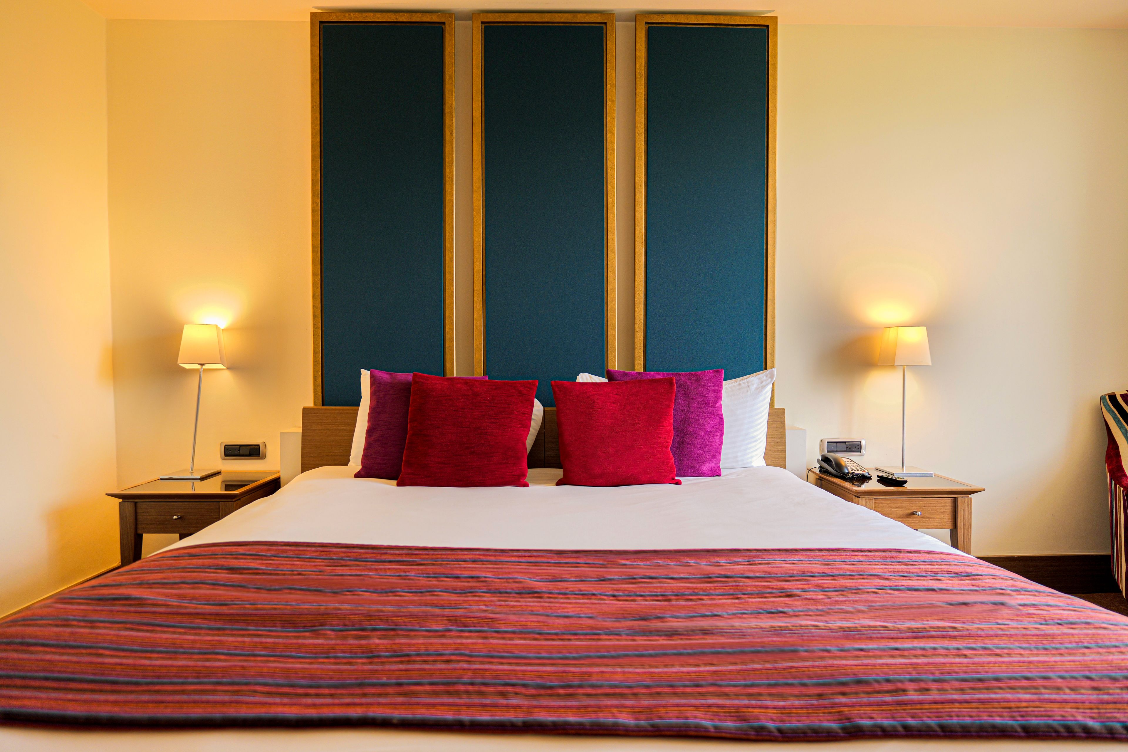 A hotel room with a large bed, two bedside lamps, a telephone, and a nightstand.