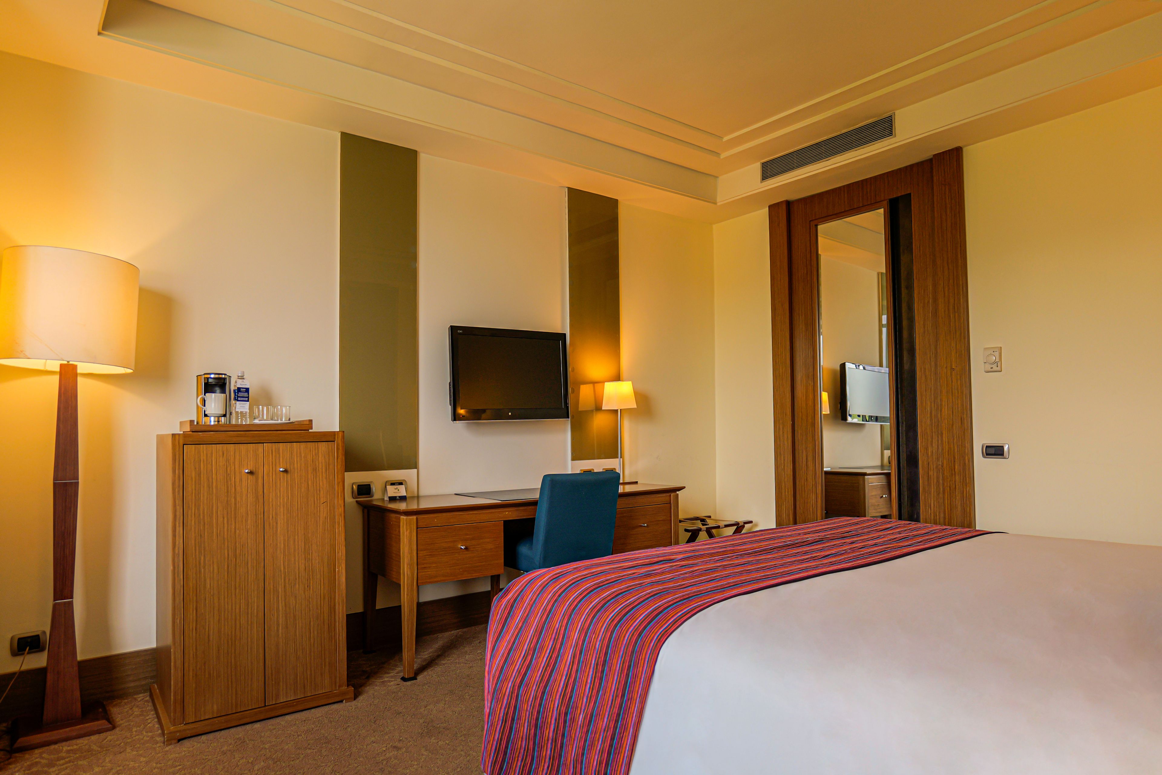 A hotel room with a bed, a desk, a chair, a television, and a wardrobe.