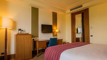 A hotel room with a bed, a desk, a chair, a television, and a wardrobe.