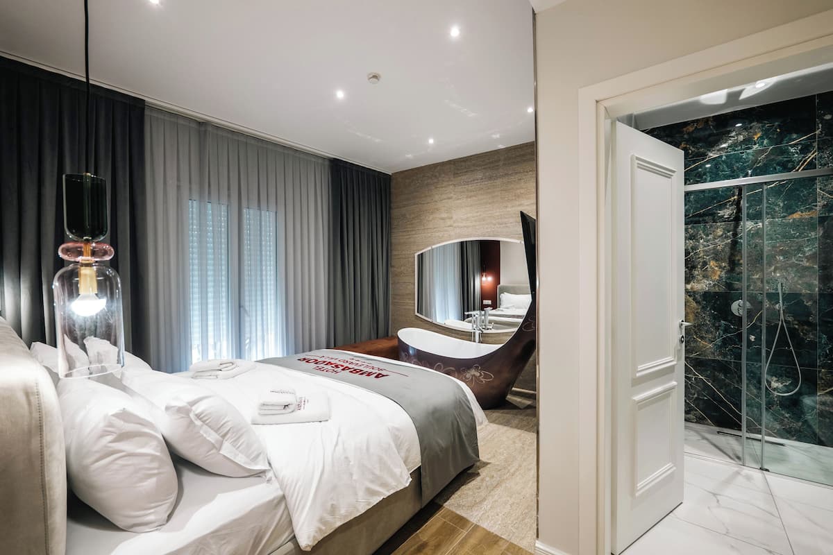 A modern hotel room with a large bed, a bathroom with a freestanding bathtub, and a glass-enclosed shower.