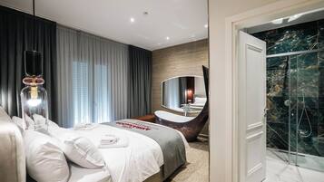 A modern hotel room with a large bed, a bathroom with a freestanding bathtub, and a glass-enclosed shower.