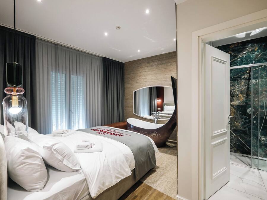 A modern hotel room with a large bed, a bathroom with a freestanding bathtub, and a glass-enclosed shower.