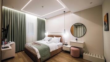 Una habitación de hotel moderna con una cama bien hecha, una mesita de noche con lámpara, un pequeño escritorio con silla y un amplio ventanal con cortinas.