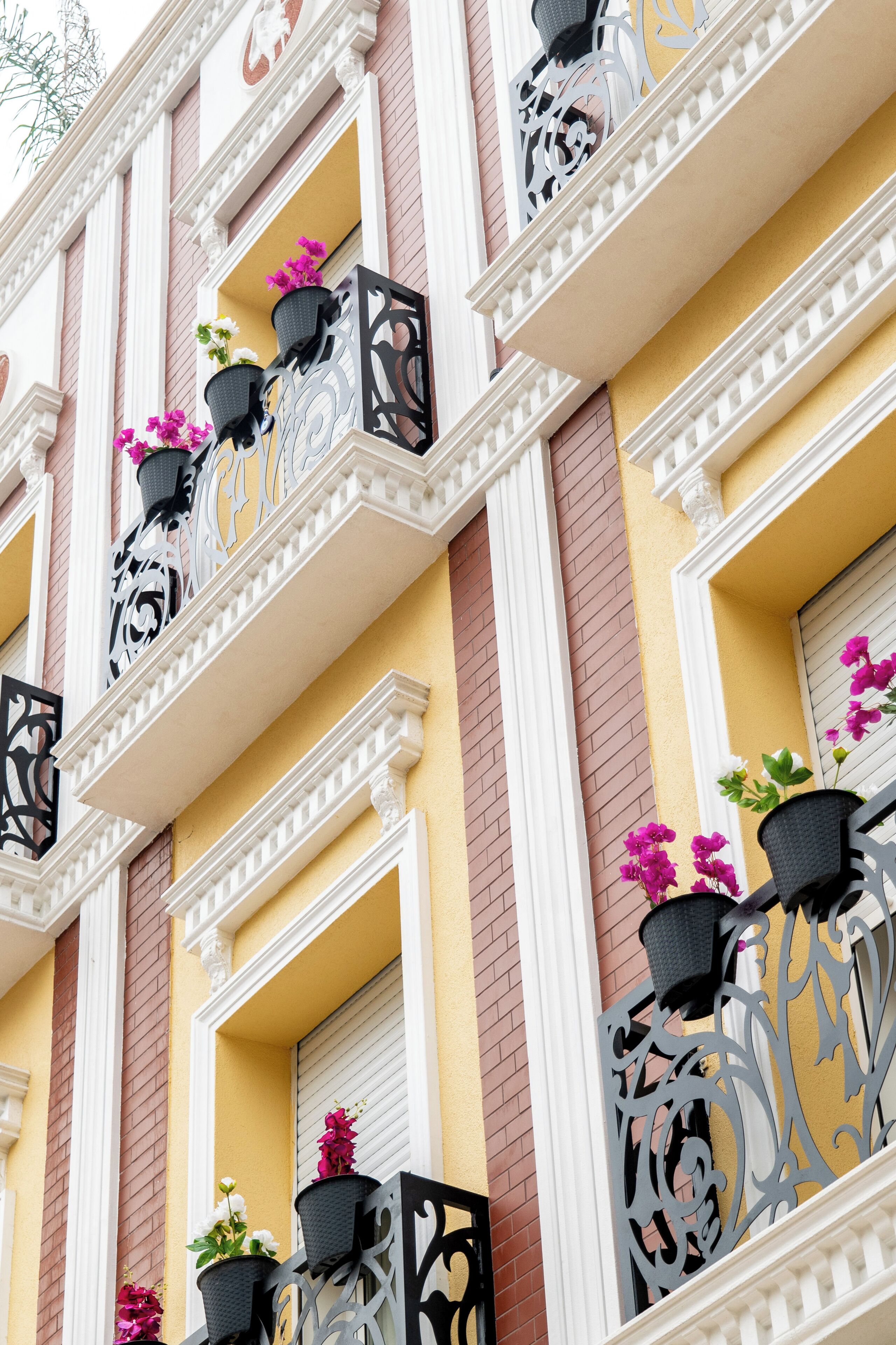 Fachada de edifício com várias varandas, cada uma com grades de metal decorativas e plantas em vasos.
