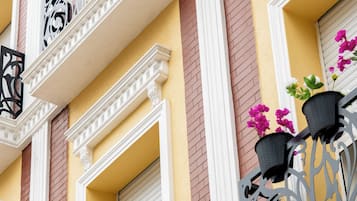 Fachada de edifício com várias varandas, cada uma com grades de metal decorativas e plantas em vasos.