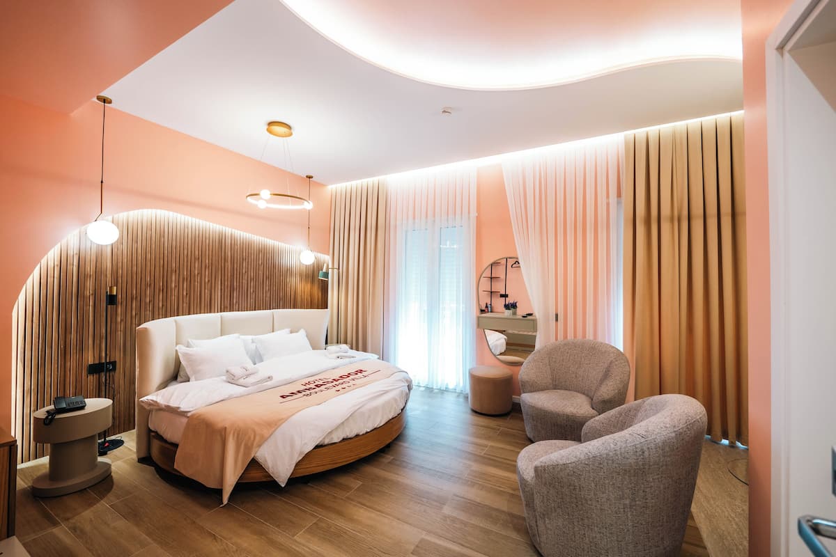 A modern hotel room with a round bed, a sitting area, and a large window with curtains.