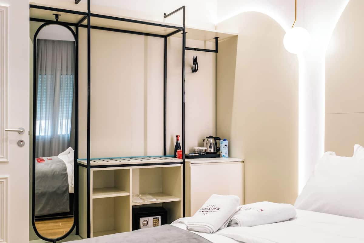 A hotel room with a bed, a desk, a mirror, and a wardrobe.