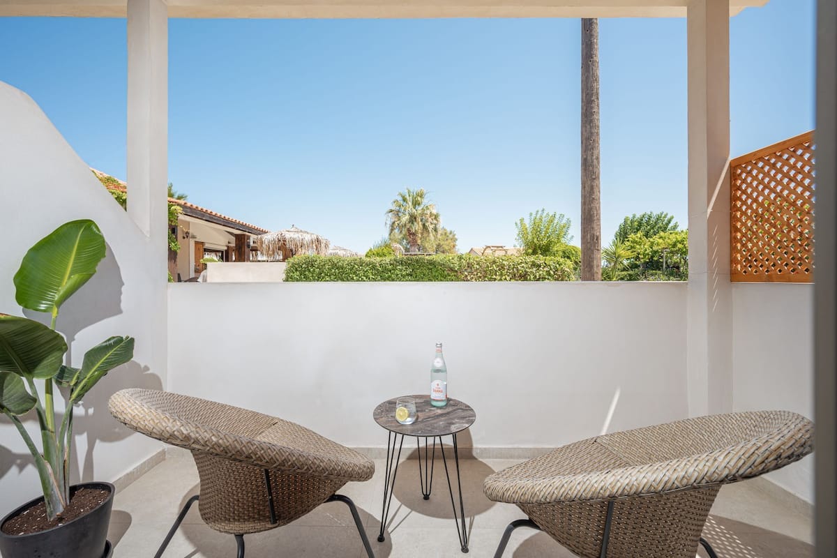A balcony with two wicker chairs, a small round table, and a bottle of Panna on the table.