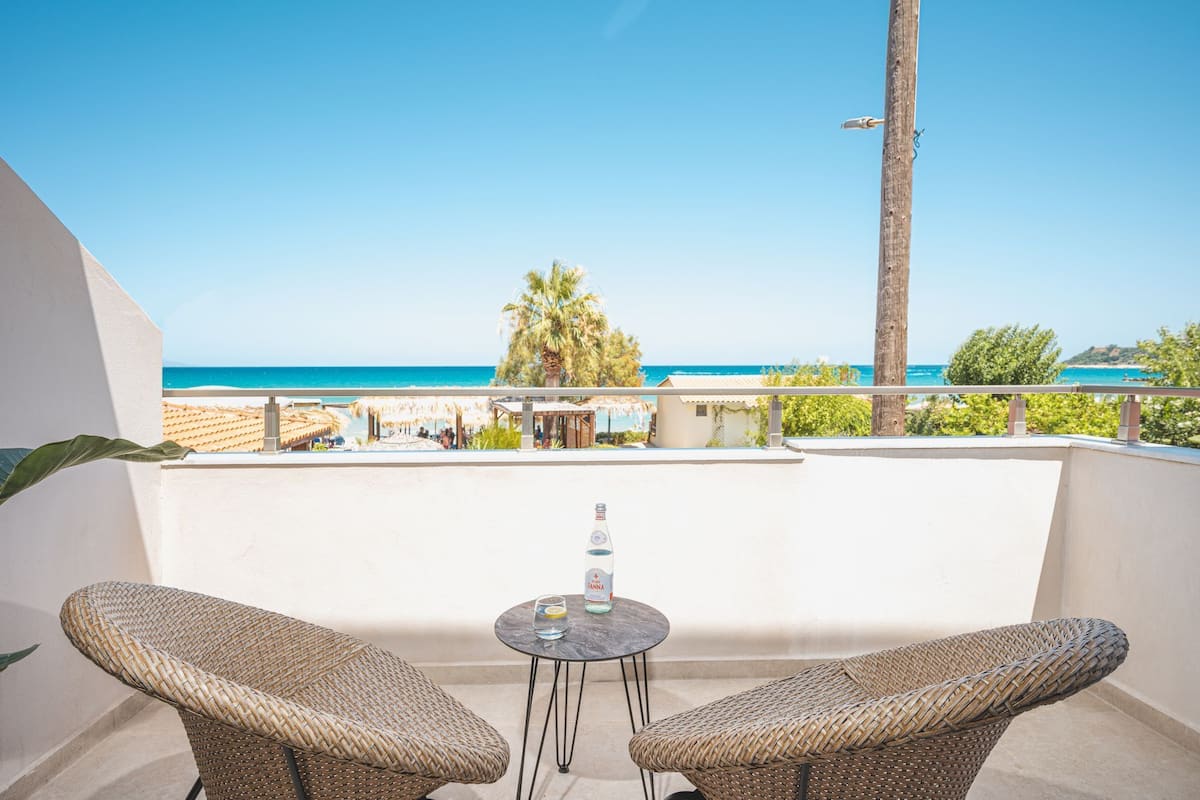 A balcony with wicker chairs, a small table with a bottle and glass, and a view of the beach and ocean.