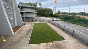 A parking lot with a green lawn area, a building with a grey facade, and a flagpole with a flag. - 1st Place at Wesley (Decatur)