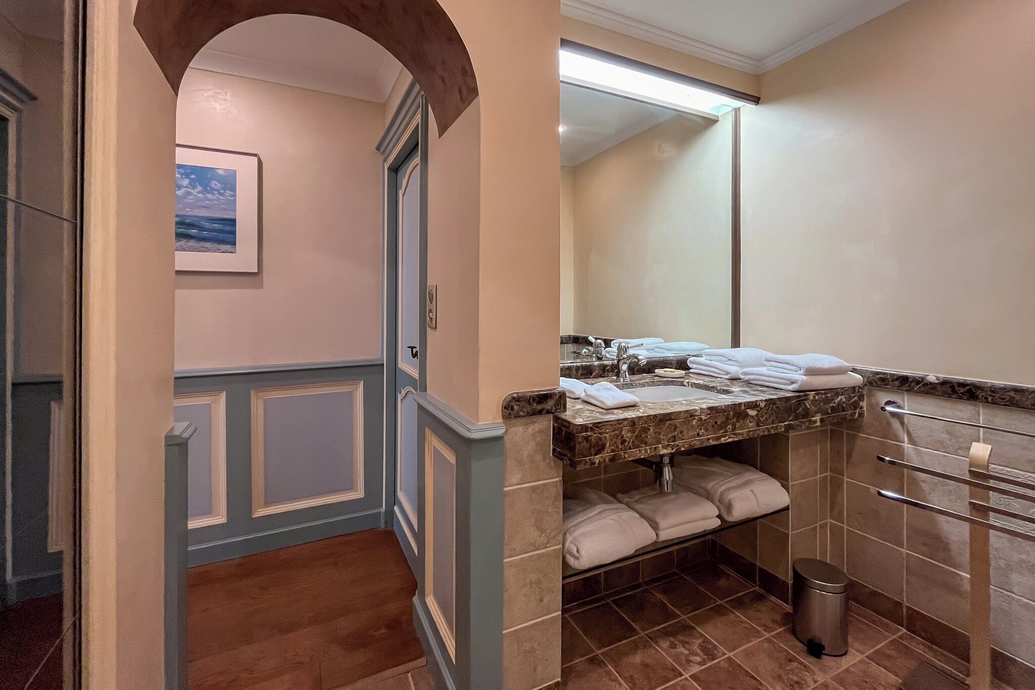 A bathroom with a marble countertop, a sink, a towel rack, and a trash can.