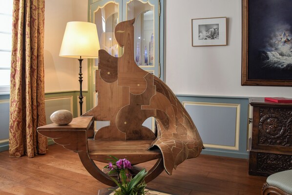 Una silla de madera de diseño único con respaldo curvo, una mesita con una lámpara y un cuadro enmarcado en la pared.