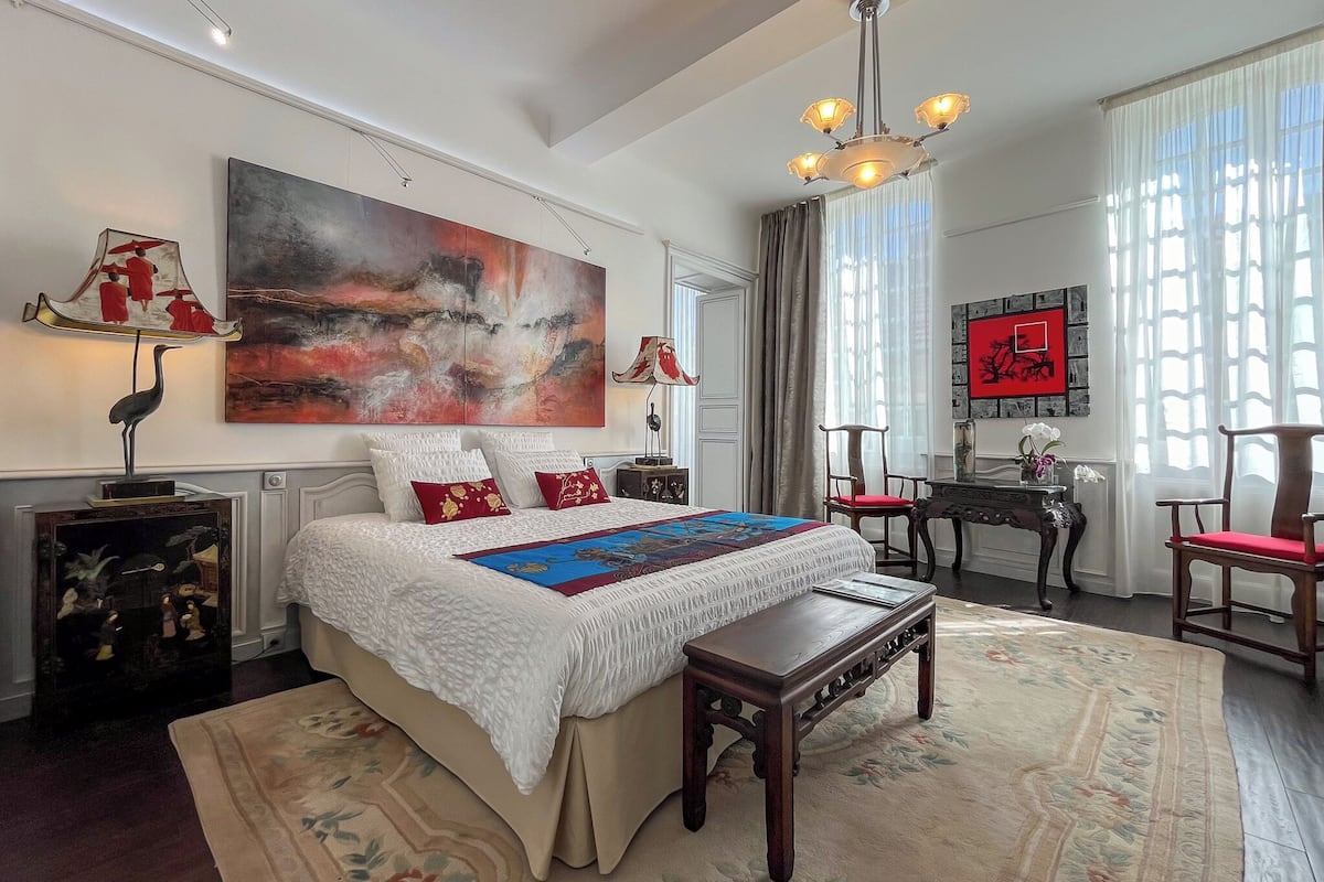 A spacious bedroom with a large bed, a wooden nightstand, a desk, and a chair.