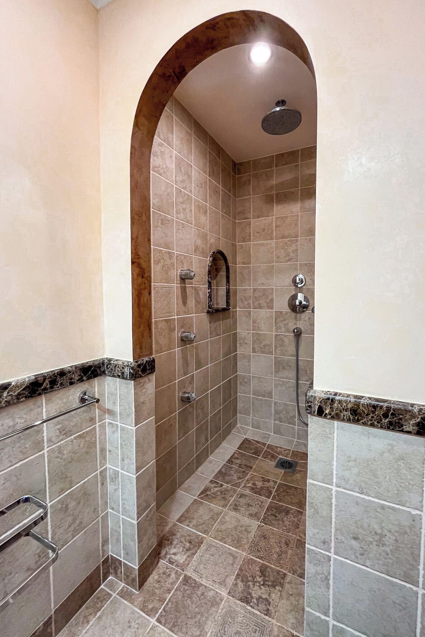 A shower with a curved arch, tiled walls, and a handheld showerhead.