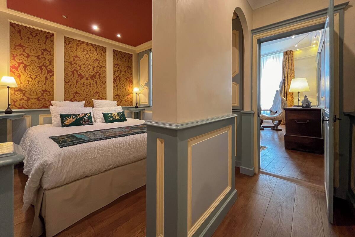 A hotel room with a large bed, two bedside tables with lamps, a dresser, and a view of the hallway.