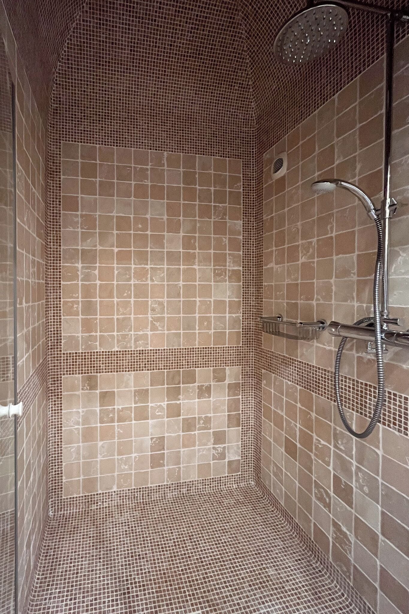 A tiled shower enclosure with a handheld showerhead and a wall-mounted faucet.