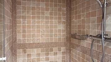 A tiled shower enclosure with a handheld showerhead and a wall-mounted faucet.