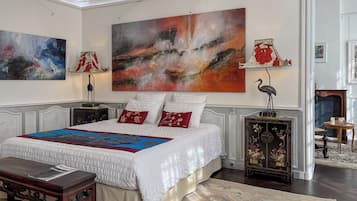 Un dormitorio amplio con una cama grande, almohadas decorativas, un cuadro abstracto de gran tamaño y una lámpara tradicional.