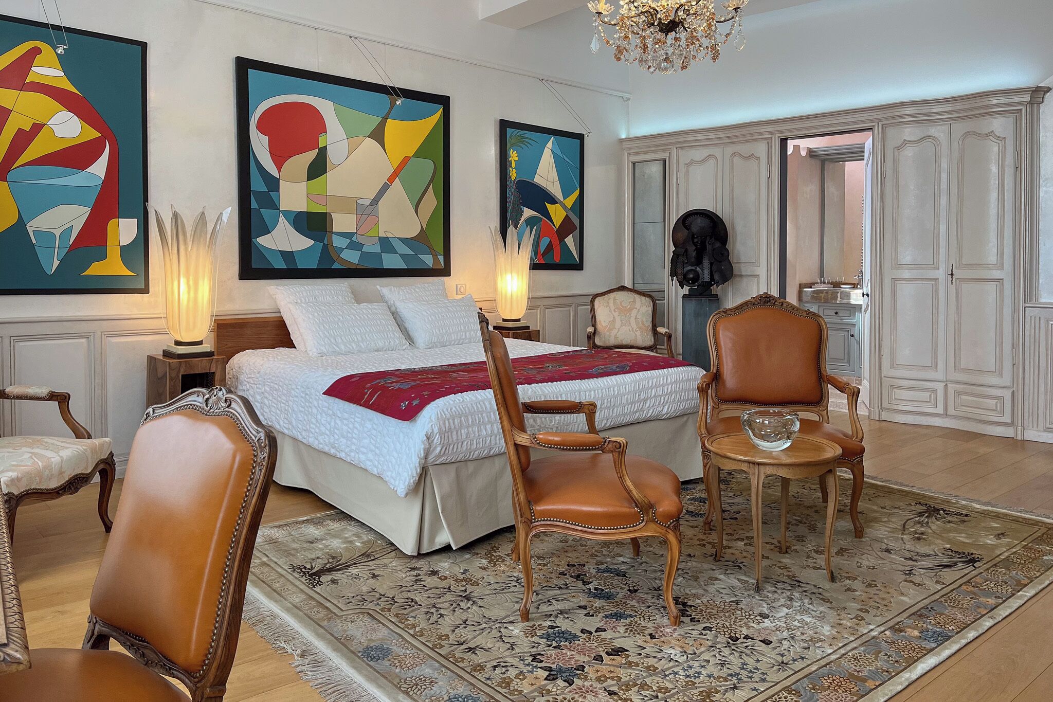 Ein Schlafzimmer mit einem großen Bett, zwei Stühlen, einem Nachttisch und Bildern an den Wänden.