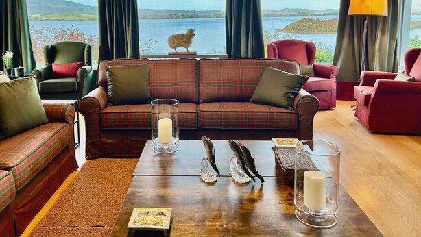 A cozy living room with a plaid sofa, a wooden coffee table with candles, and a view of a lake and hills.