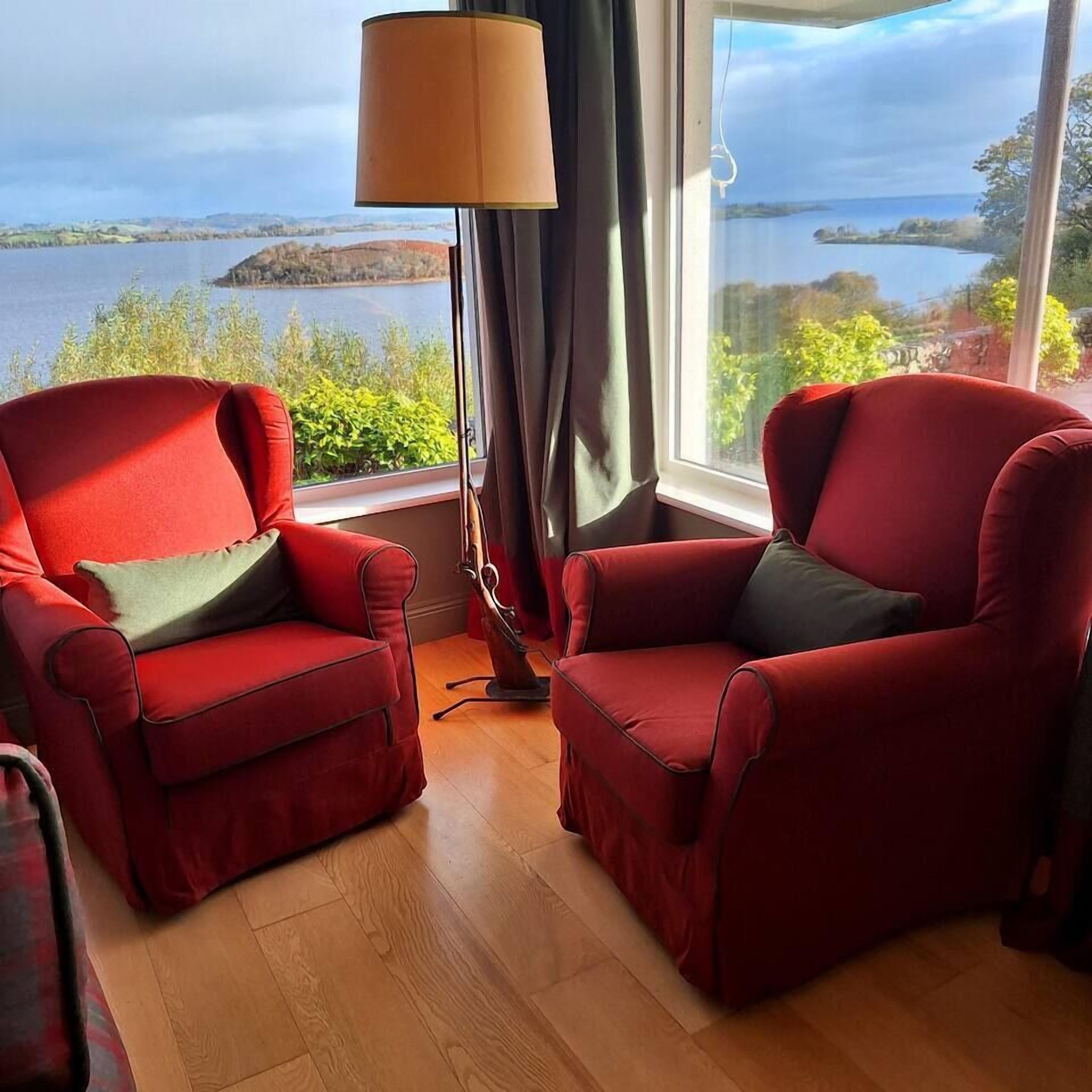 Two red armchairs facing a large window with a view of a lake and distant land.