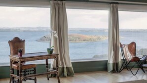 A room with a view of a lake, a wooden table with chairs, and a window with curtains.