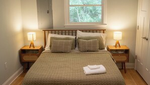 A neatly made bed with a green quilt, two bedside lamps, and a window with a view of trees. - Home in Carrboro, Fully Renovated! (Carrboro)