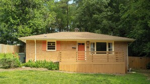 A small brick house with a wooden deck, a front door, and a mailbox. - Home in Carrboro, Fully Renovated! (Carrboro)