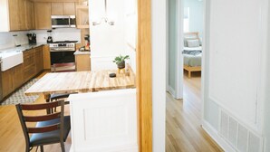 A modern kitchen with wooden cabinets, a dining table, and a view into a bedroom. - Home in Carrboro, Fully Renovated! (Carrboro)
