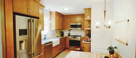 A kitchen with wooden cabinets, stainless steel appliances, a dining area with a table and chairs, and a hanging light fixture.