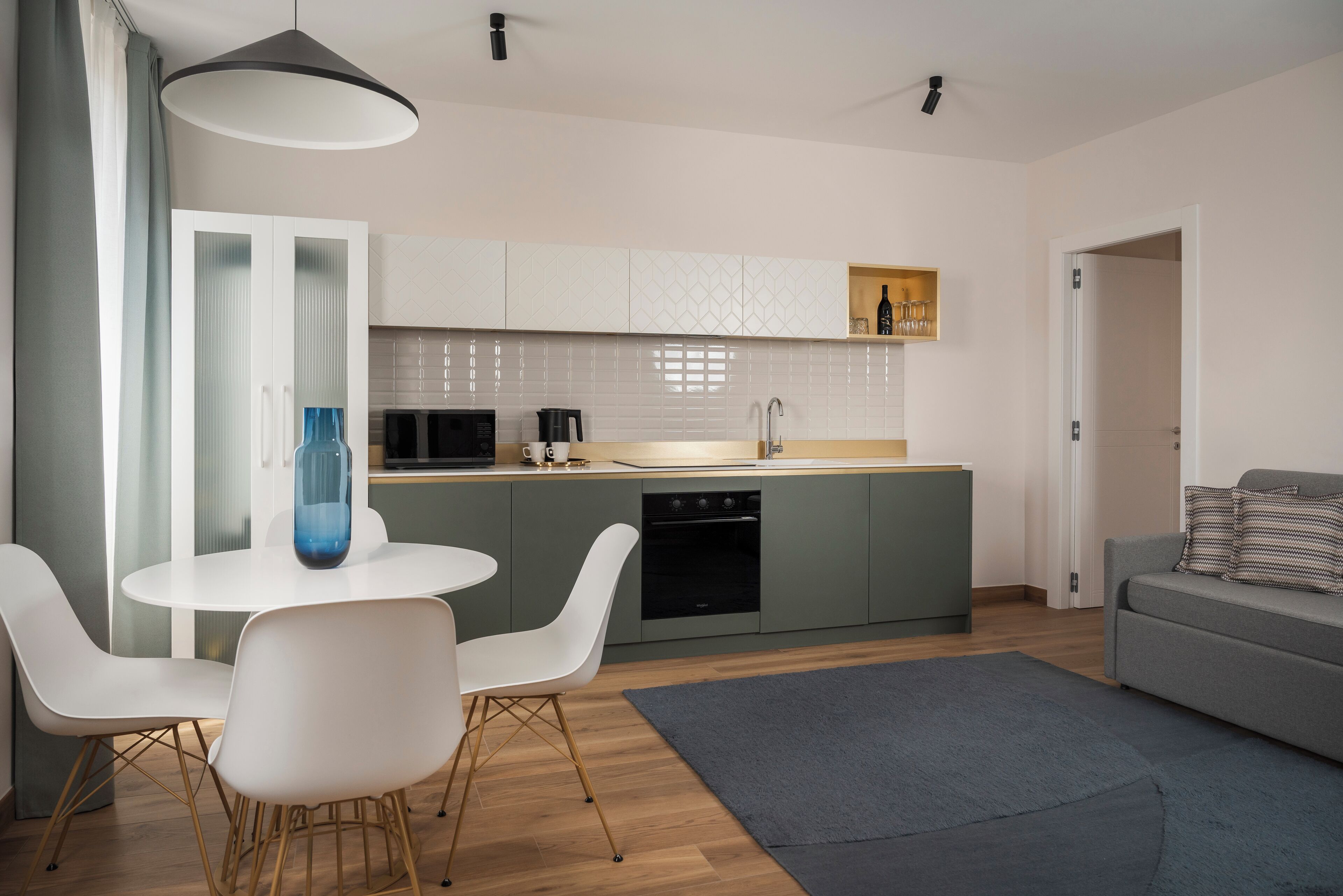 A modern kitchen with white cabinets, a central island, and a dining area with white chairs.