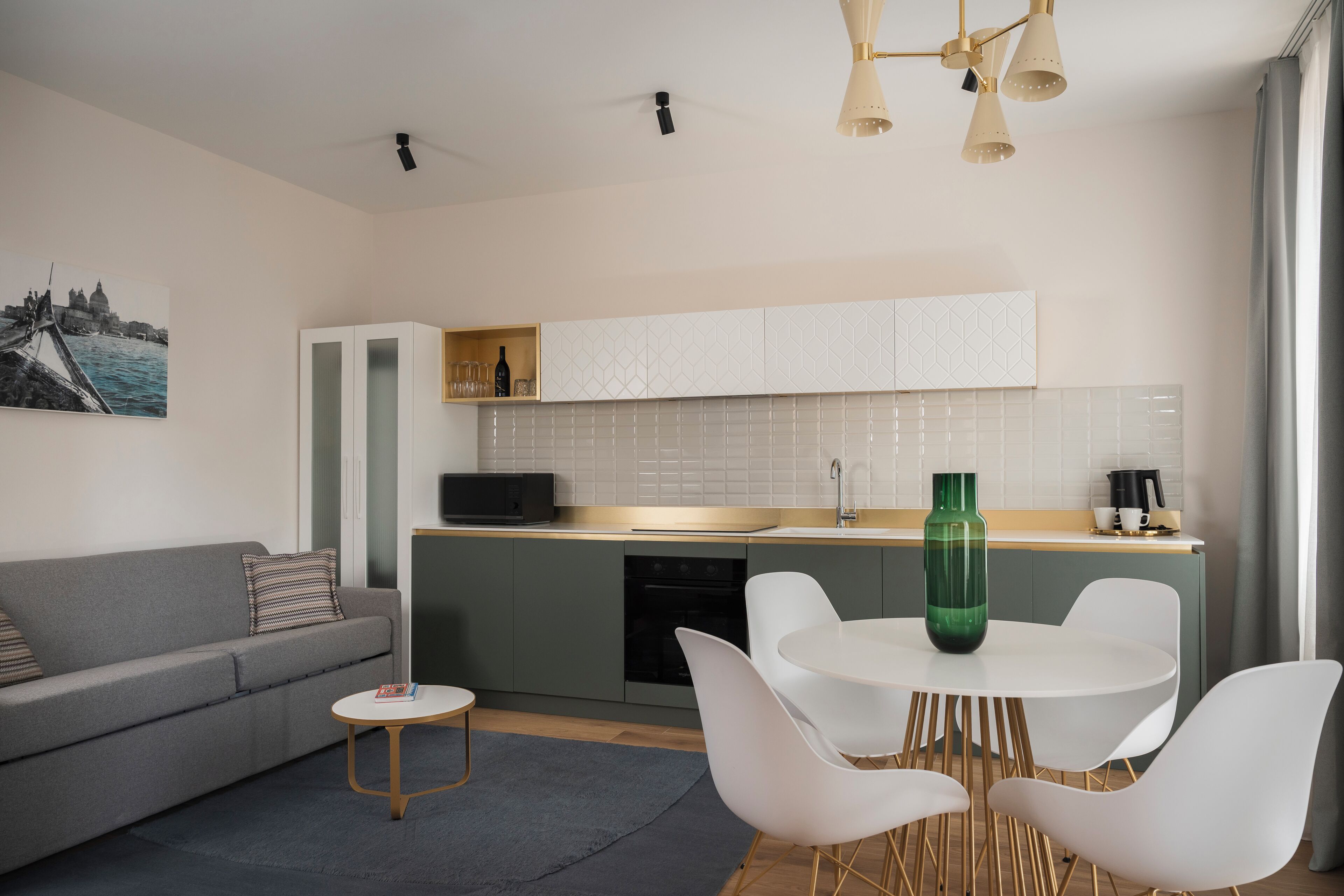 A modern kitchen with white cabinets, a dining area with a round table and white chairs, and a grey sofa.