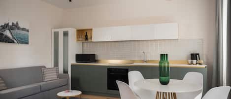 Una cocina moderna con armarios blancos, un comedor con una mesa redonda y sillas blancas, y un sofá gris.