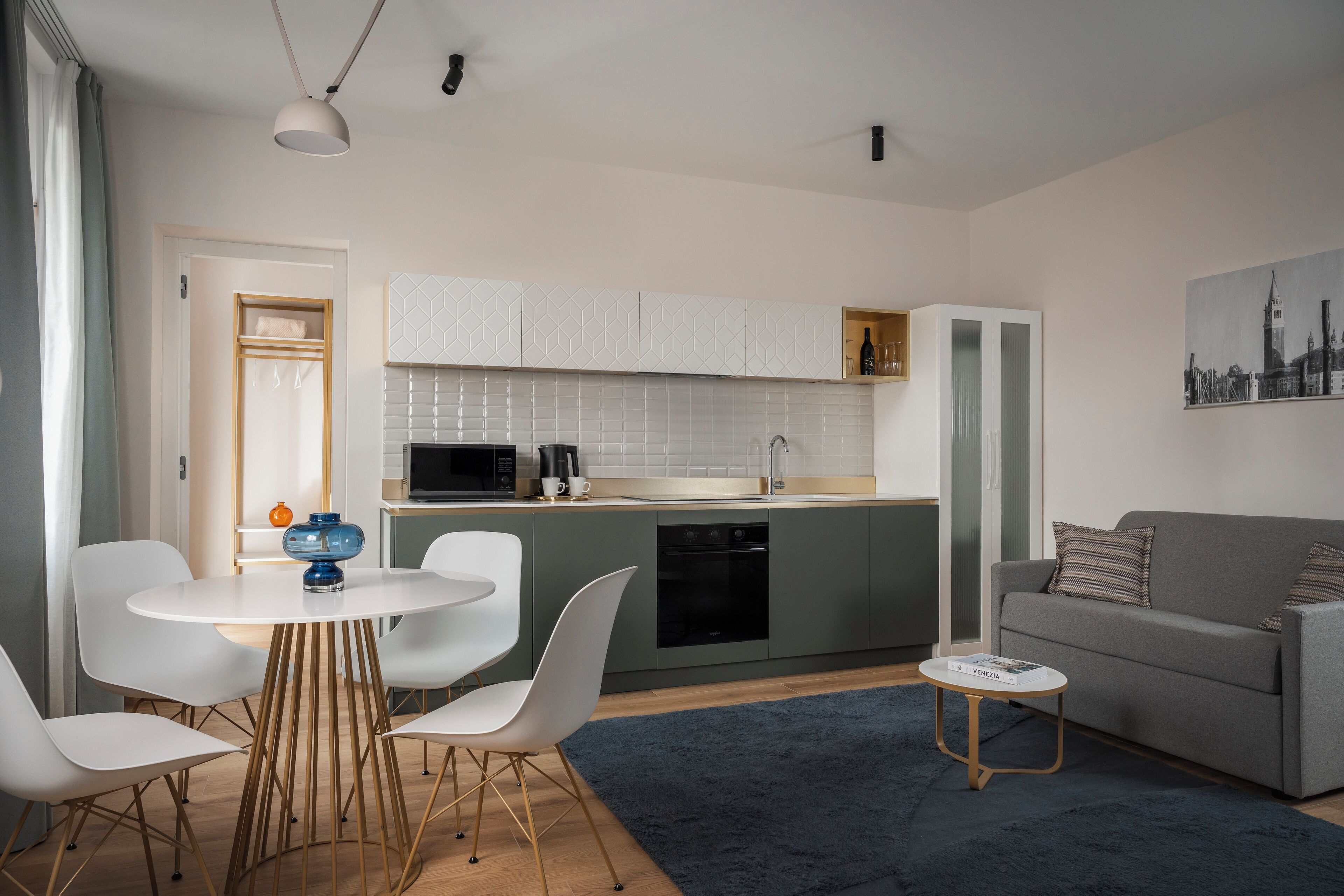 A modern kitchen with white cabinets, a dining area with a round table and chairs, and a grey sofa.