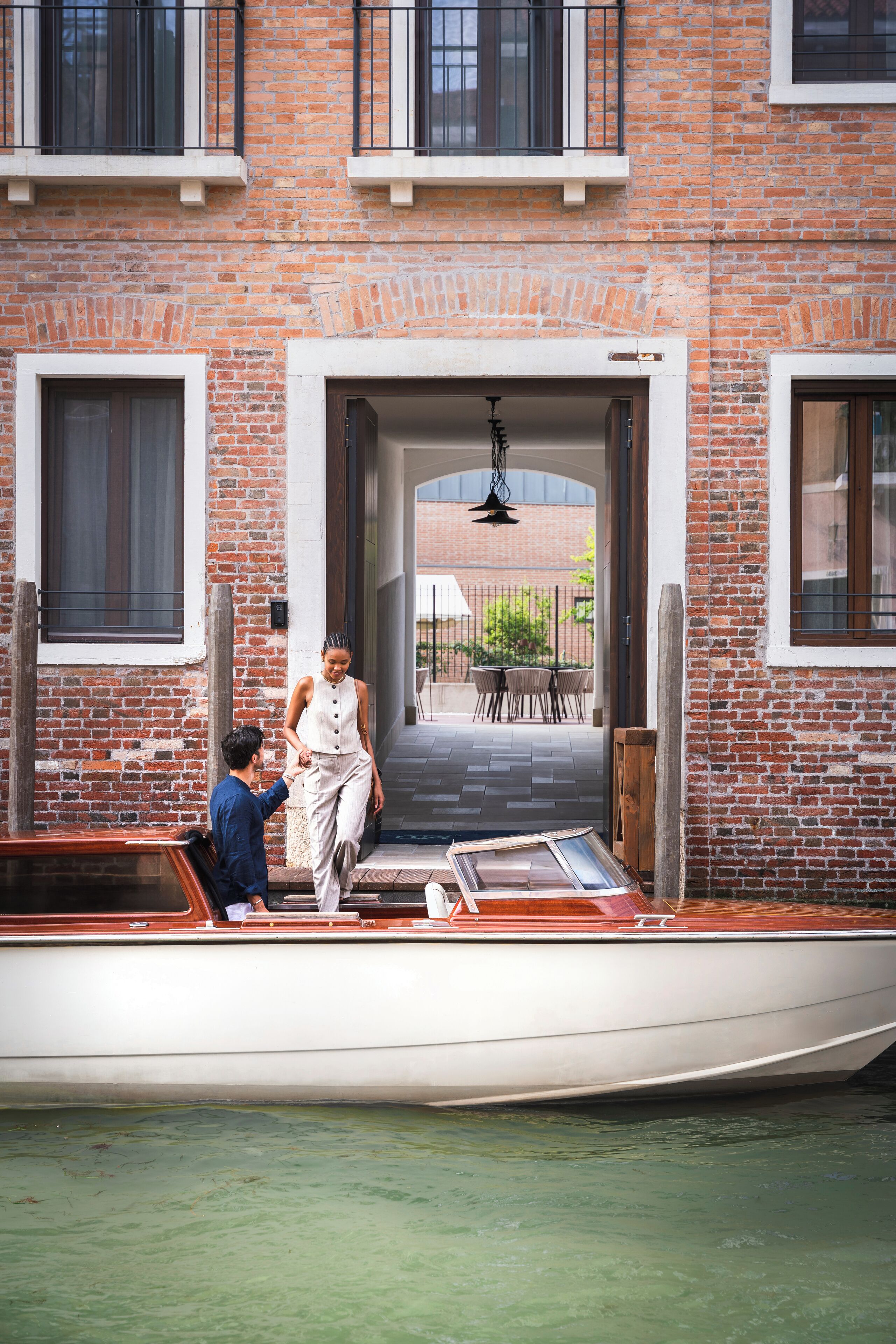 A boat docked at a building with a brick facade, a door leading to an outdoor area, and a clear view of the water.