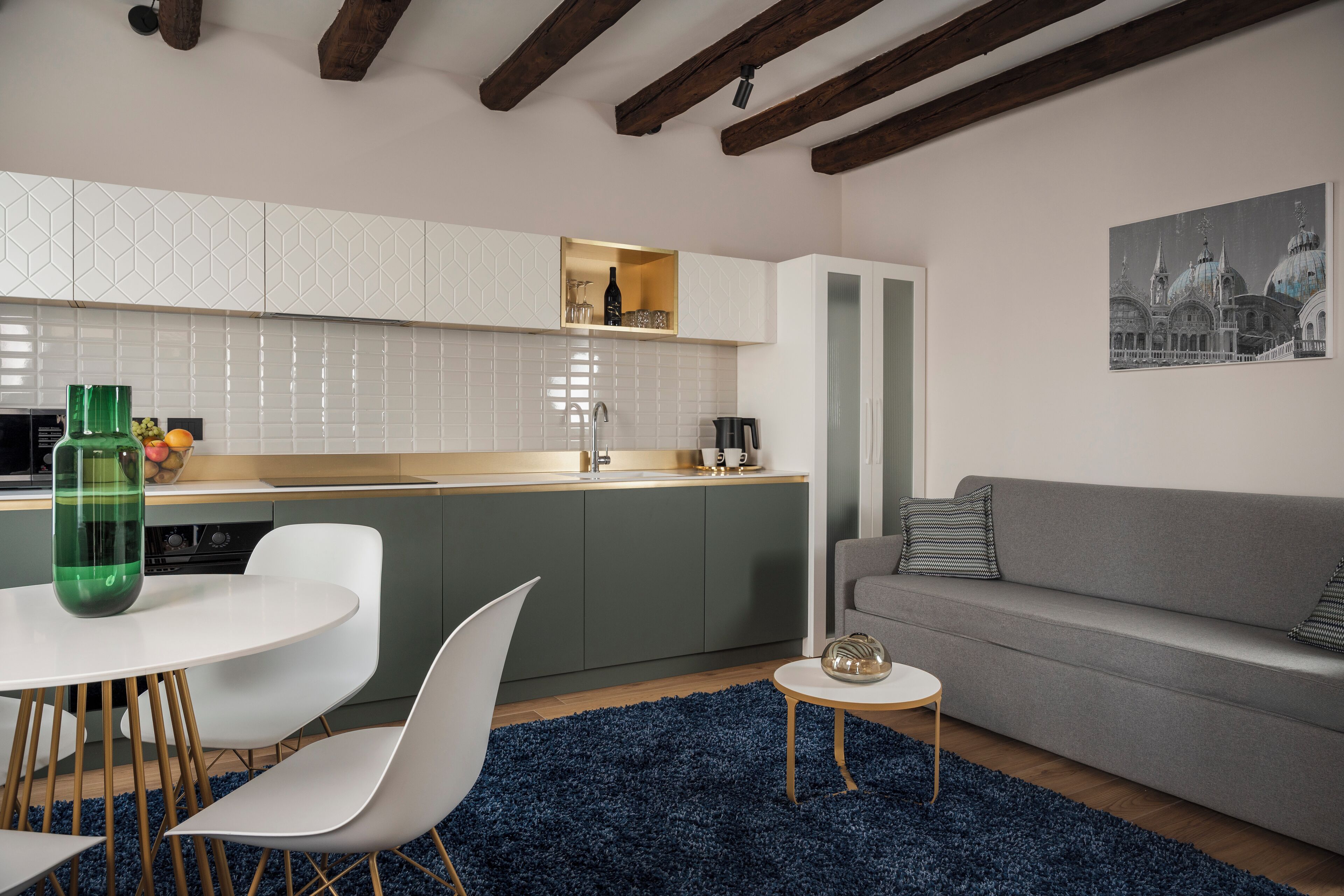 A modern kitchen with white cabinets, a dining area with white chairs, and a grey sofa.