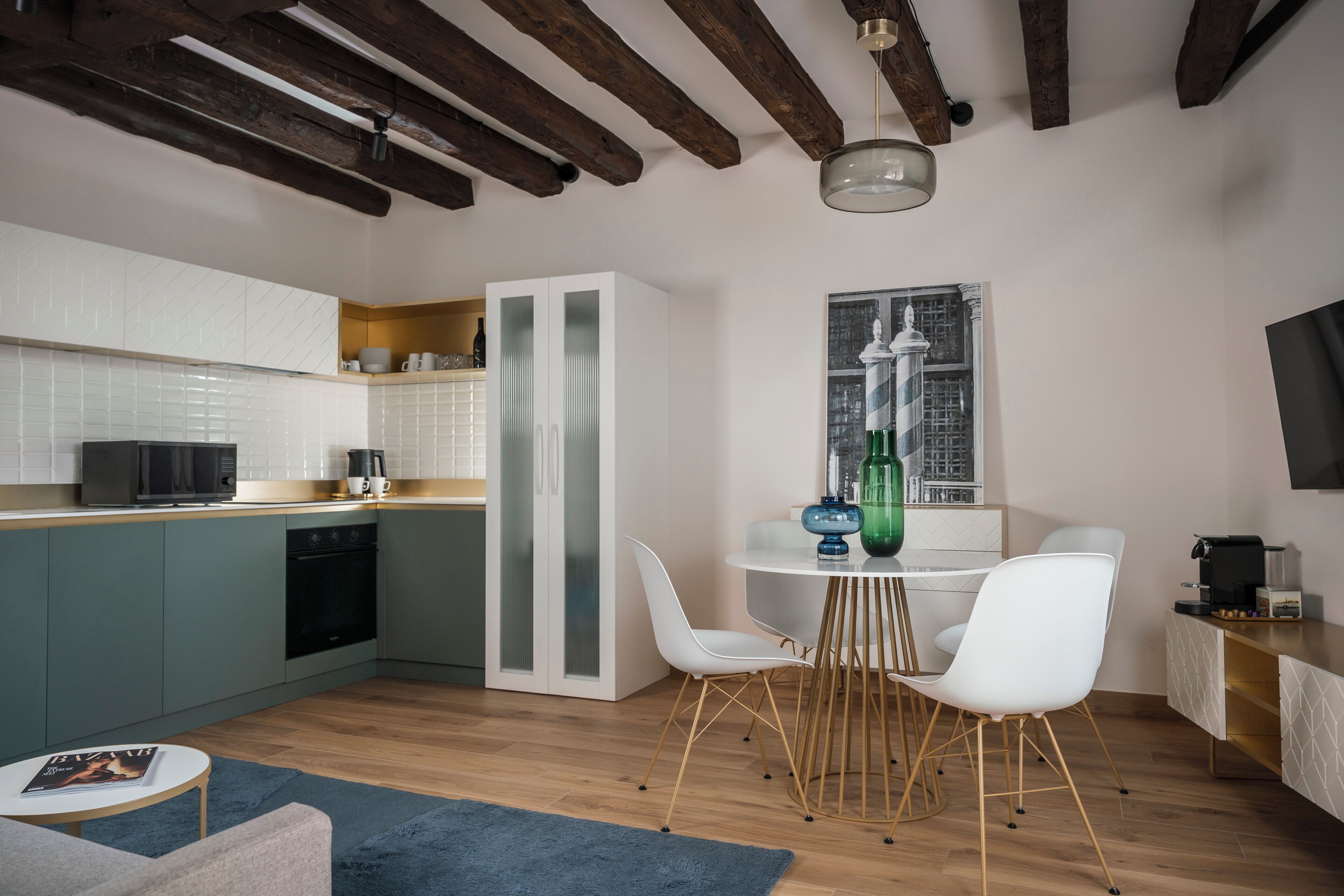 A modern kitchen with white cabinets, a built-in oven, and a dining area with white chairs and a round table.