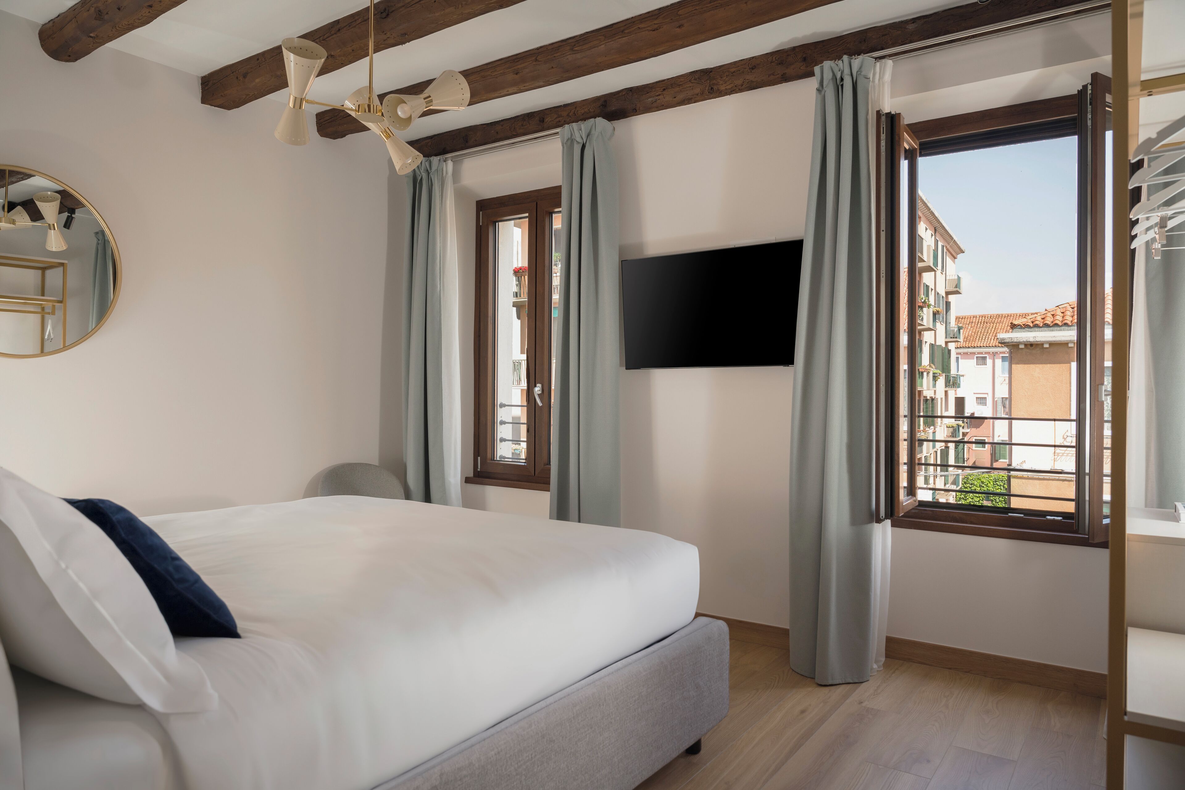 Een slaapkamer met een bed, een aan de muur bevestigde televisie en een raam met gordijnen.