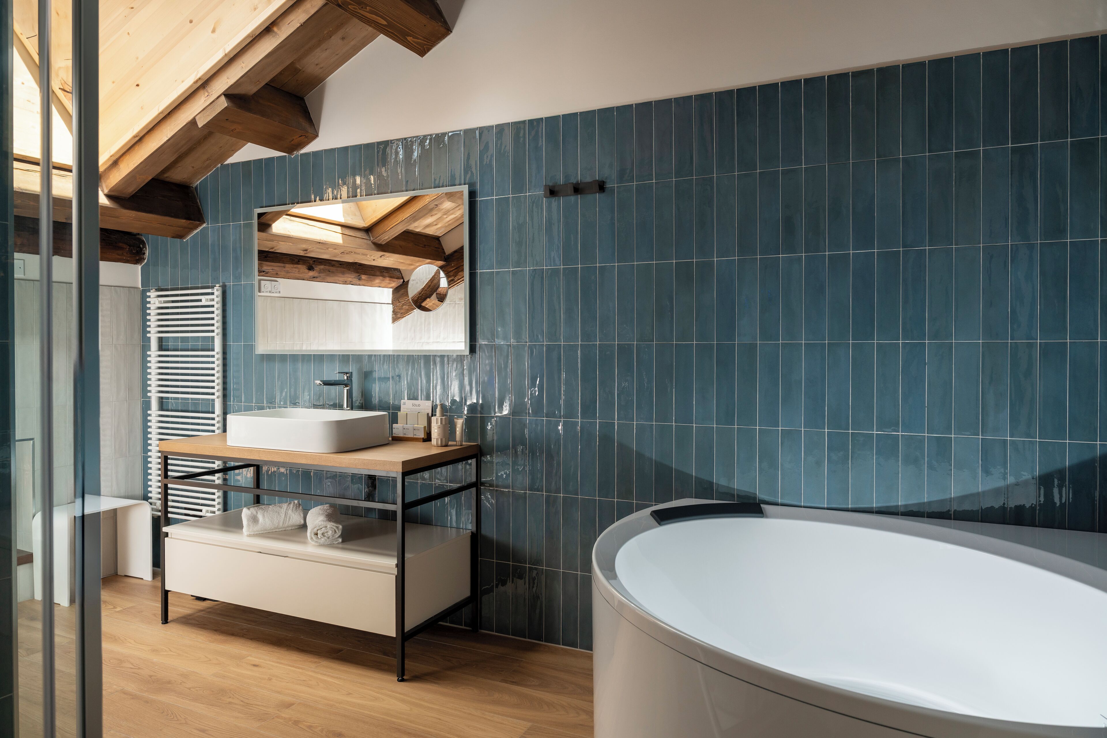 Un baño moderno con una bañera independiente, un lavamanos con espejo y un banco de madera.