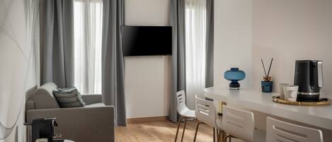 Una sala de estar moderna con un sofá, una mesa de centro, un televisor montado en la pared y un comedor con sillas y una máquina de café.