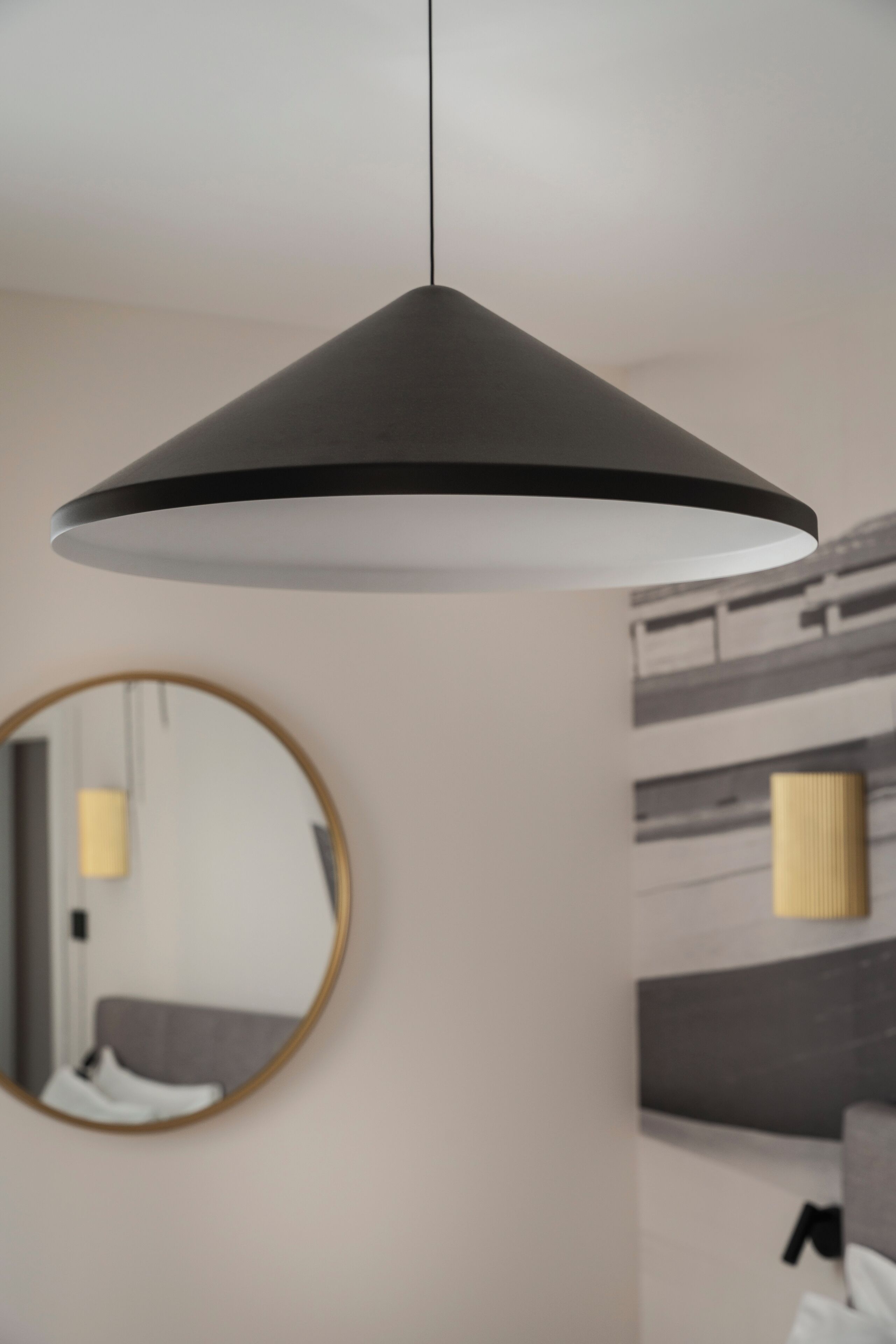 Une chambre moderne avec un miroir rond, un lit doté d’une tête de lit grise et un luminaire suspendu.