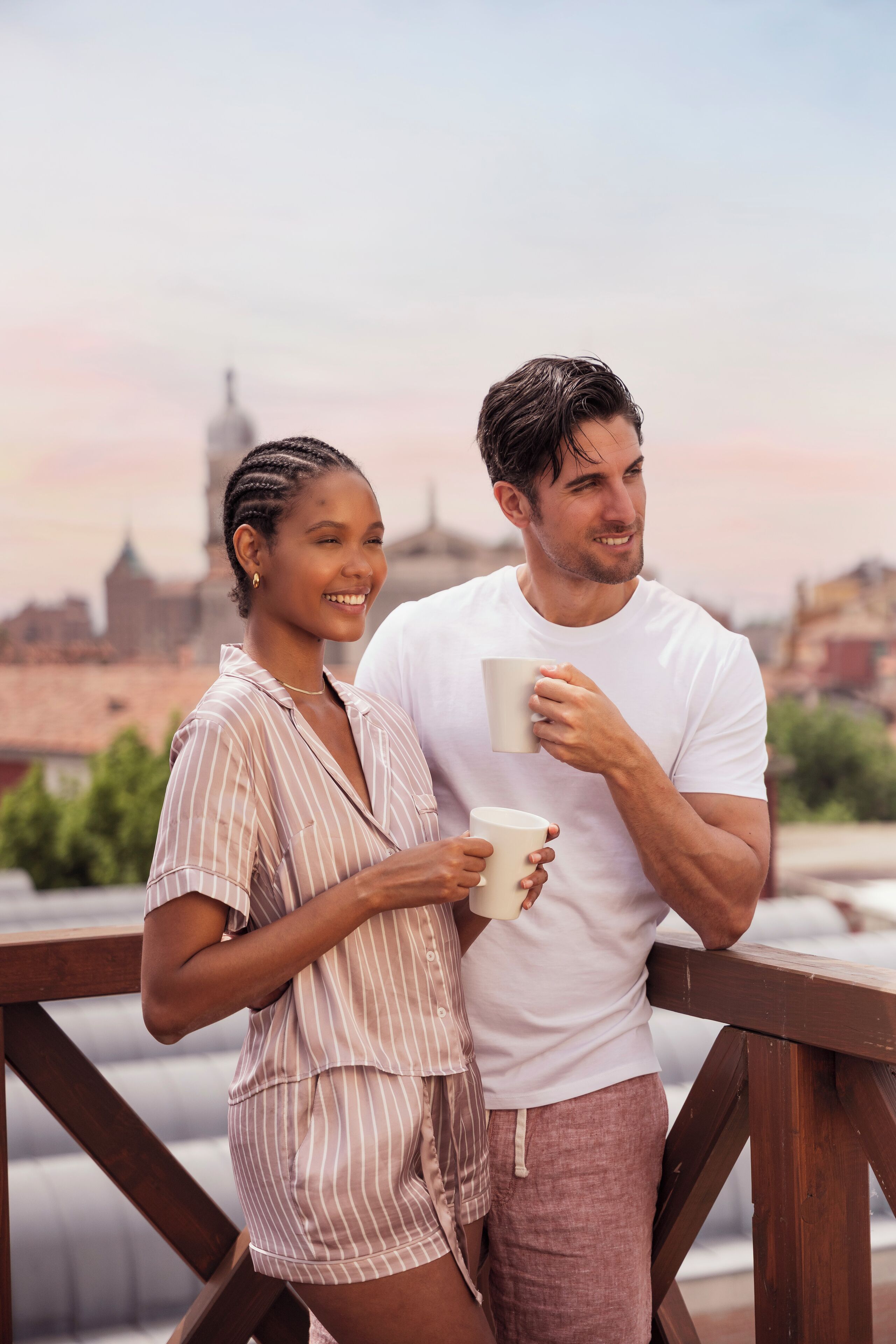 A couple standing on a balcony with a cityscape in the background.